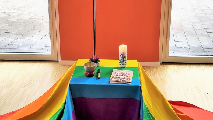 Ein bunter Tisch mit Kreuz, Kerze und Bibel vor einem Fenster