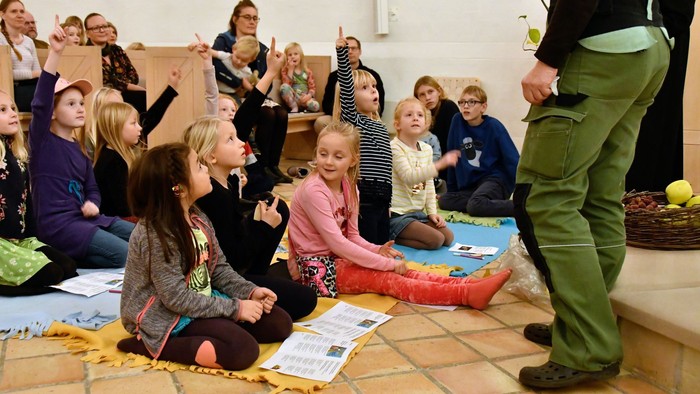 Børn deltager i en interaktiv og engagerende gruppeaktivitet ledet af en instruktør, hvor de sidder på måtter med papirer.