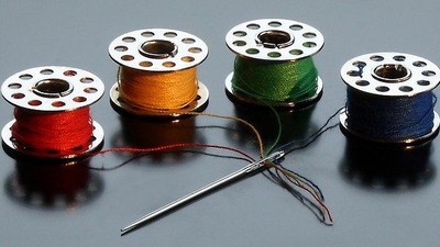Vier Spulen mit bunten Fäden und eine Nadel