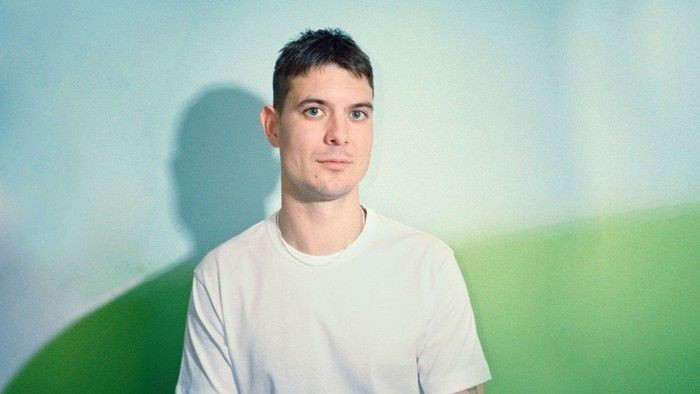 En person i en almindelig hvid t-shirt, der poser foran en gradient grøn baggrund.