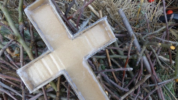 Ein Holzkreuz liegt auf einem Haufen Zweige und Blätter.
