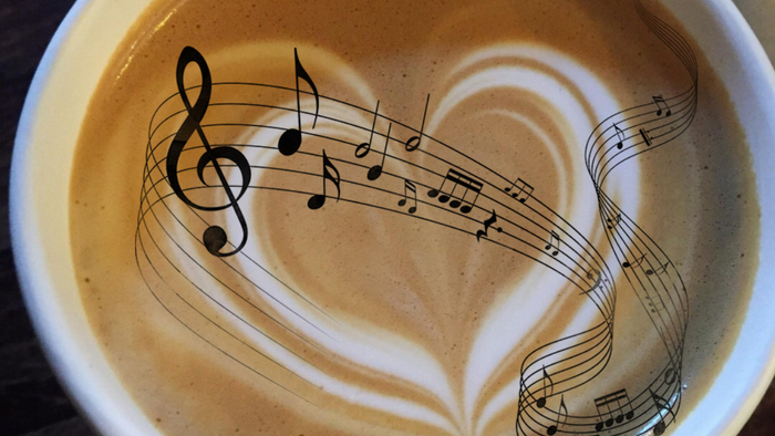 Ein Latte Macchiato in einer Tasse mit einer Herzen- und Notenmotiv aus Milchschaum