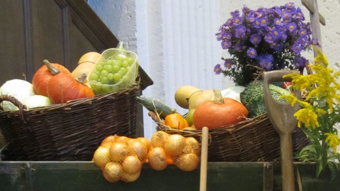 Kutsche mit Gemüse und Blumen vor weißer Wand