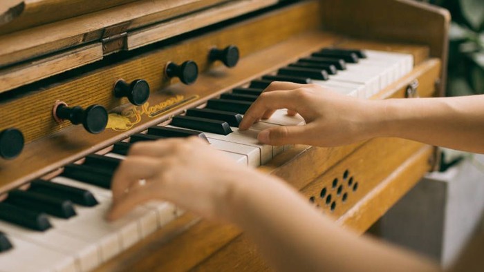 Eine Person spielt Klavier, die Hände berühren die Tasten.