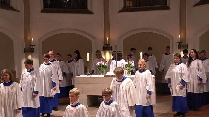 Ein Chor aus Kindern und Erwachsenen in weißen Roben mit blauem Besatz singt während einer Zeremonie in einer Kirche.