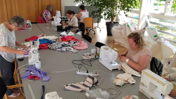 En gruppe håndværks-sy-session med forskellige symaskiner, stoffer og materialer spredt ud over et bord.