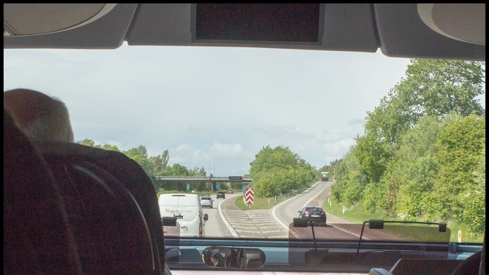 En chauffør ser en motorvej med skiltning om vejarbejde og køretøjer forude på en solskinsdag.