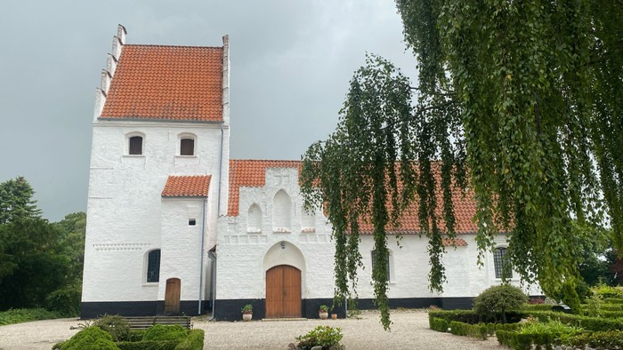 Et hvidt kloster med røde tag og en indhegnet have med buske og træer