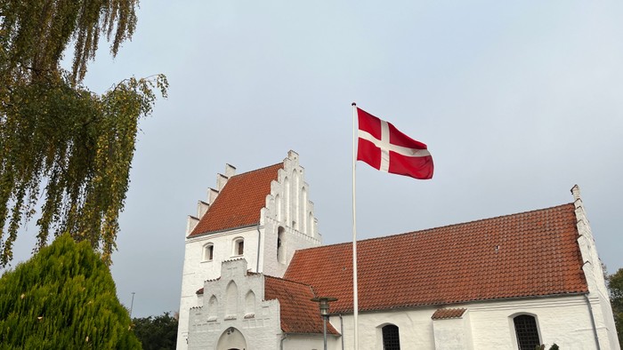 En hvid kirke med røde tag og en dansk flag på en stang foran