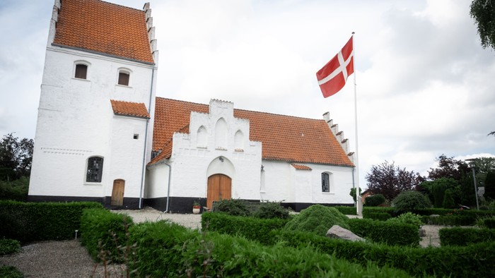 Hvid kirke med røde tag og dansk flag på tårn