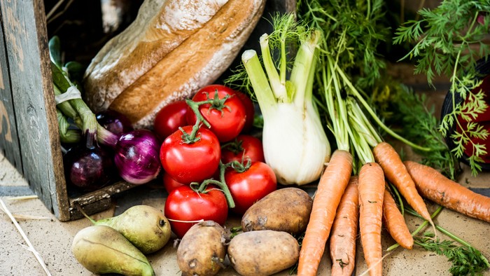 En samling af ferske grøntsager, heriblandt tomater, kartofler, rødbede og gulerødder, udstillet på en bjælke og en murstenet vegg
