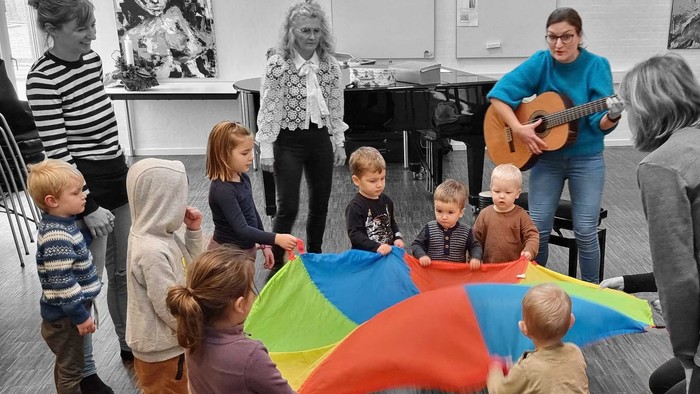 Børn der danser med voksne omkring sig. En af de voksne spiller guitar