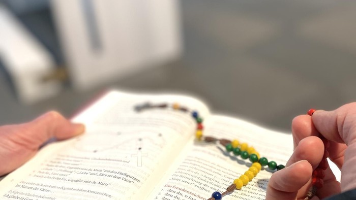 Person hält ein offenes Buch und eine Perlenkette