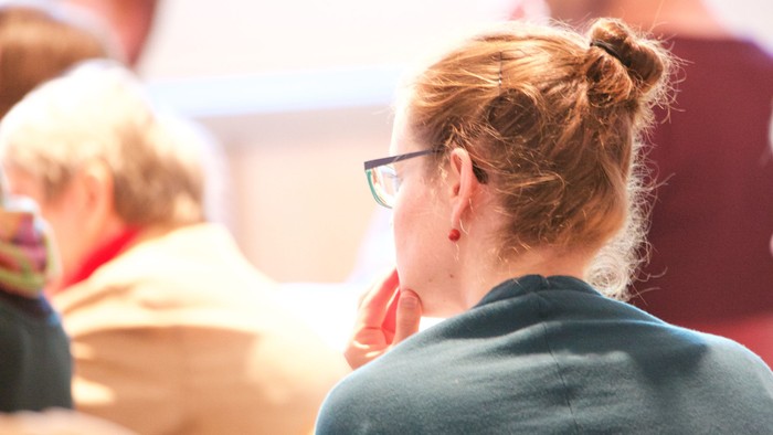 Eine Person mit Dutt und Brille wendet sich in einer belebten Umgebung von der Kamera ab.