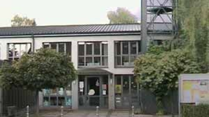 Das Bild zeigt ein modernes Gebäude mit einem hohen Turm und umgeben von Bäumen.