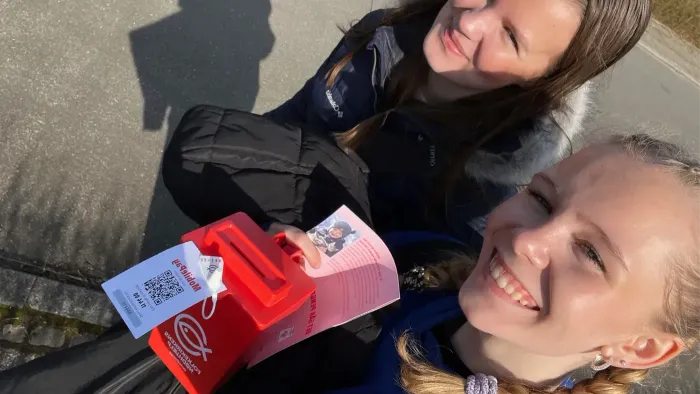 To glade mennesker, der sidder udendørs og holder en rød æske med en QR-kode og et kort.