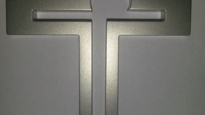 Ein metallisches Kreuz an einer grauen Wand.