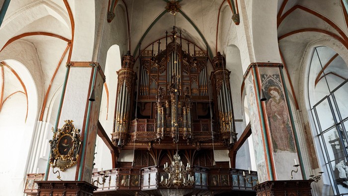 Historische große Pfeifenorgel in einem prunkvollen, gewölbten Kircheninnenraum mit hölzernen Kirchenbänken und dekorativen Wandmalereien.