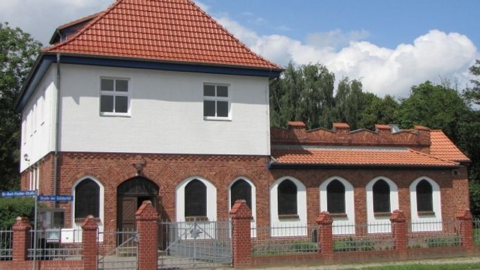 Weißes Gebäude mit rotem Dach und Turm, umgeben von einem Zaun