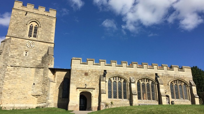 Stone church with tall tower and arched windows under blue sky.