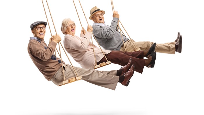 Drei ältere Männer sitzen lachend auf einer Schaukel.