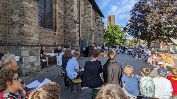 Open-Air-Chorprobe vor einem alten Steingebäude mit vielen Teilnehmern.