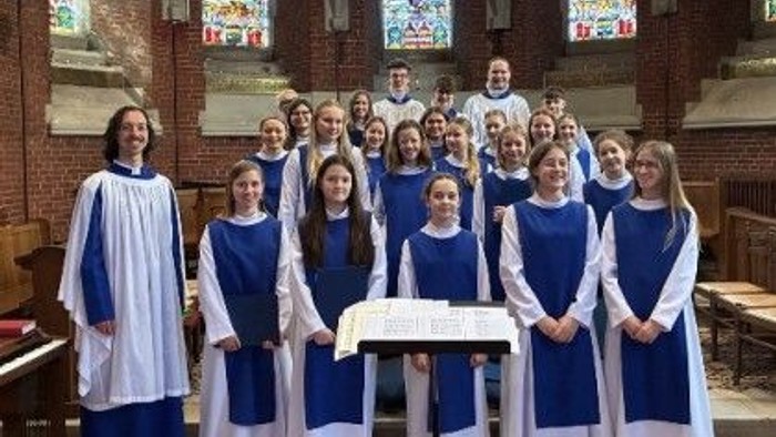 Ein Jugendchor in blau-weißen Roben posiert gemeinsam in einer Kirche mit bunten Kirchenfenstern.