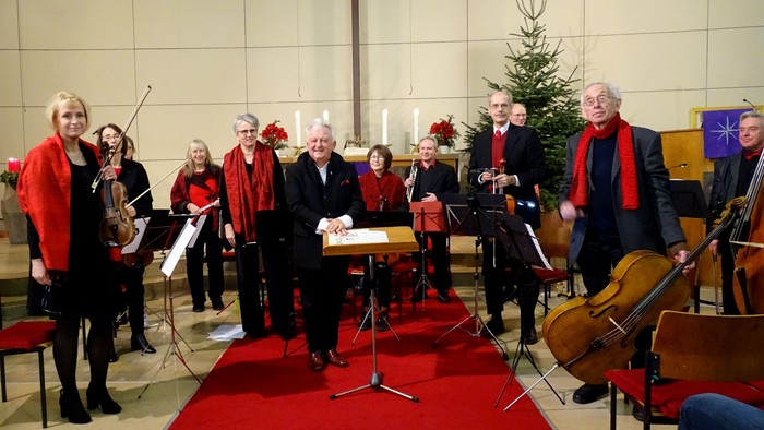 Ein Kirchenchor proben mit Musikern und Notenständern vor einem Kreuz und Weihnachtsbaum