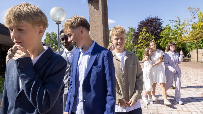 En gruppe studerende i formelt tøj, der går udendørs på en solskinsdag.