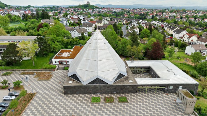 Modernes Gebäude mit Pyramidendach in Wohngebiet mit vielen Häusern und Grünflächen.