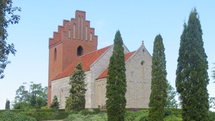 En park med formede hegge og høje træer med et rødt tårn i baggrunden