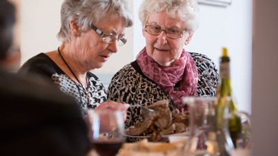 To eldre kvinder sidder ved bord og ser på mad.