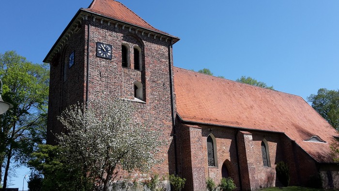 Das Bild zeigt eine alte Kirche mit einem hohen Turm und einem Ziegeldach.