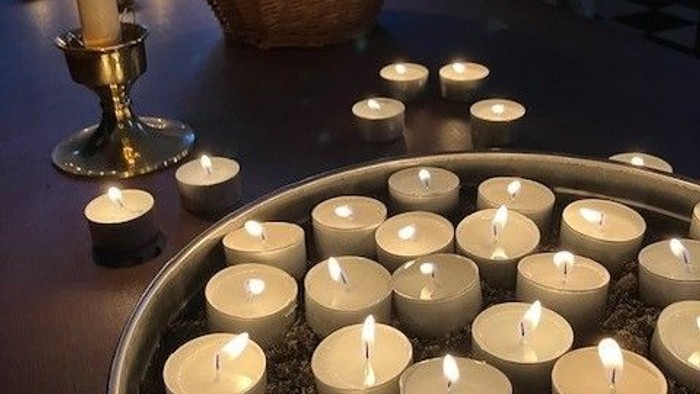Arrangerede stearinlys i forskellige holdere skaber en varm, rolig lyssætning på et mørkt bord.