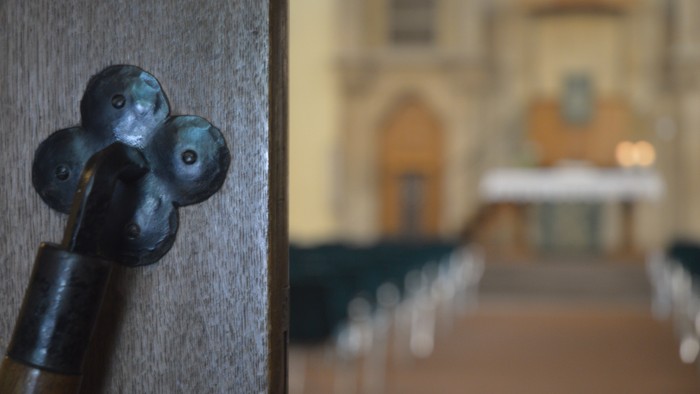 Links ein altes Türschloss, rechts eine Kirchenbankreihe