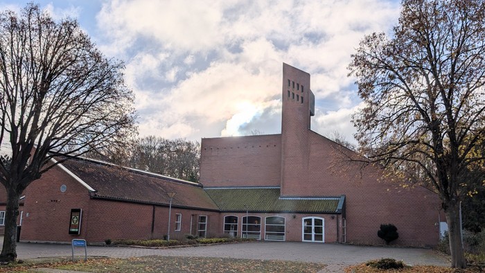 Et rødt teglsteinsbygning med tårn og træer foran