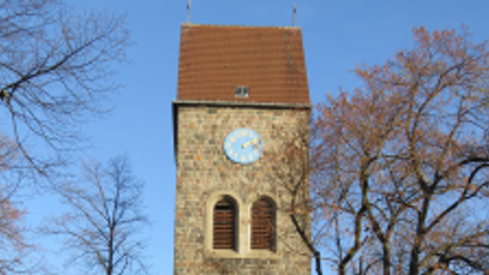 Alter Kirchturm mit Uhr und buntem Glasfenster, umgeben von Bäumen