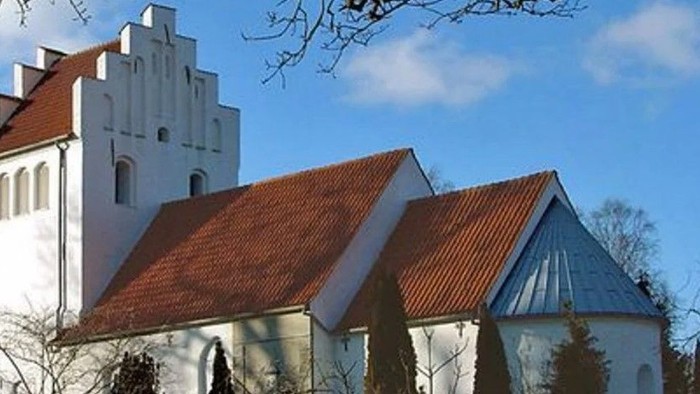 Et hvidt kirkebygningskompleks med røde tag og en tårn.