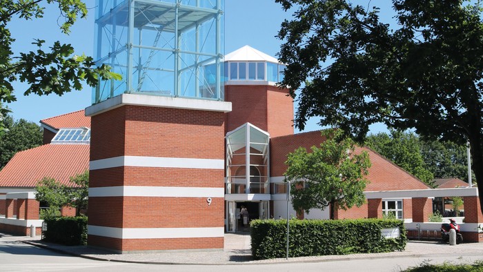 Et moderne glasbygning i en parkagtig omgivelse