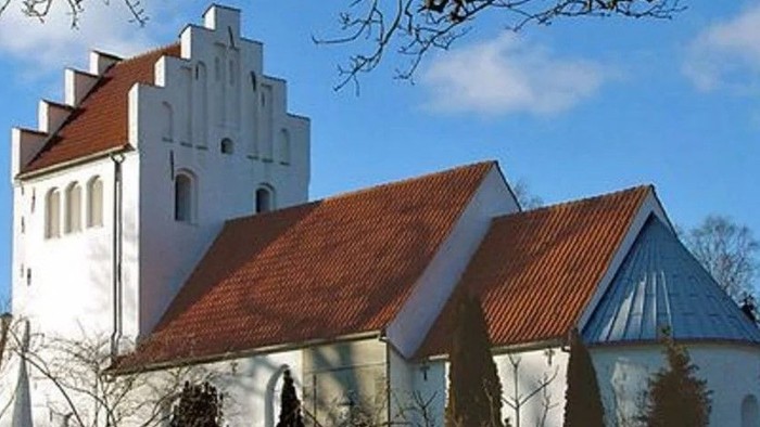 Et hvidt kirkebygningskompleks med røde tag og en tårn.