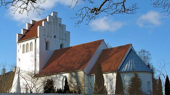 Et hvidt kirkebygning med røde tag og en klokketårn i en snedækked landskab