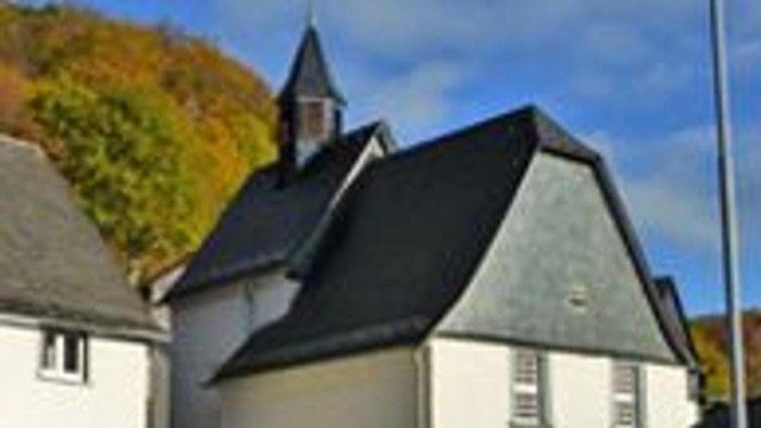 Kleine weiße Kirche mit schwarzem Dach, umgeben von Herbstbäumen.