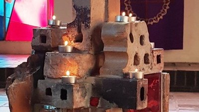 Auf einem Tisch stehen Kerzen in einer Steinskulptur vor einem farbenfrohen Hintergrund