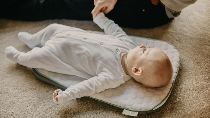 En baby ligger på et puslebord, mens en voksen forsigtigt holder dens hånd.