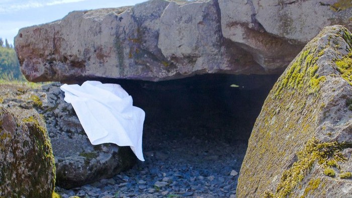 Ein weißes Tuch hängt in einer Felshöhle am felsigen Ufer.