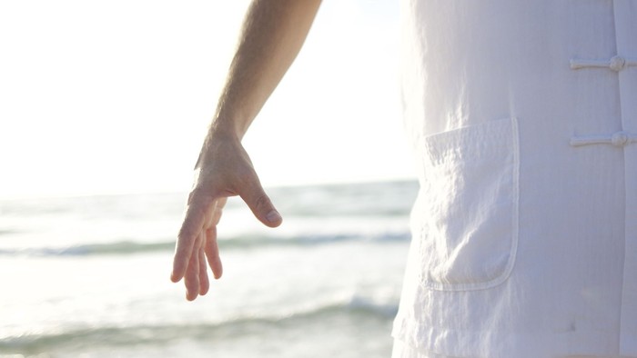 Eine Person am Strand mit ausgestrecktem Arm, Sonnenlicht im Hintergrund