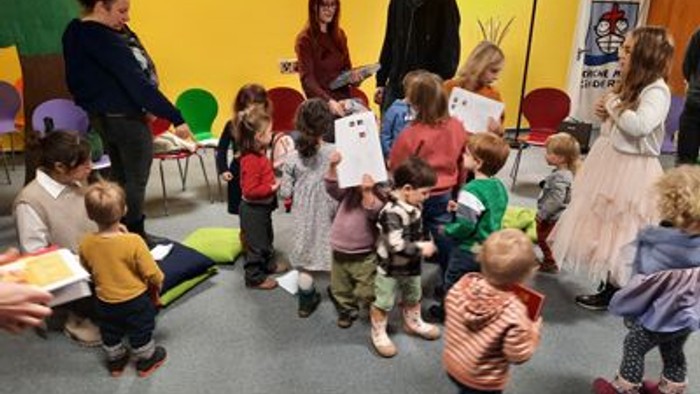 Kinder nehmen an einer Gruppenaktivität mit Erwachsenen teil, die Schilder in einem bunten Innenraum-Klassenzimmer halten.