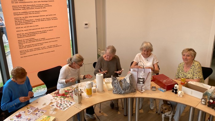 Gruppe älterer Menschen, die um einen Tisch sitzen und einer Bastelaktivität nachgehen.