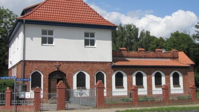 Weißes Gebäude mit rotem Dach und Turm, umgeben von einem Zaun