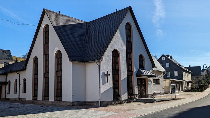 Weiße Kirche mit schwarzem Dach und Kreuz an der Fassade